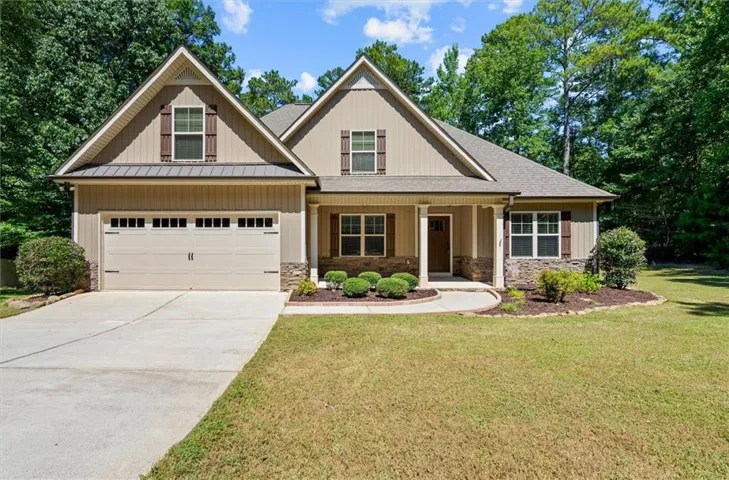Gabled roofline with shake siding accents, stone veneer foundation, covered entry porch, attached garage with decorative hardware, and mature perimeter trees