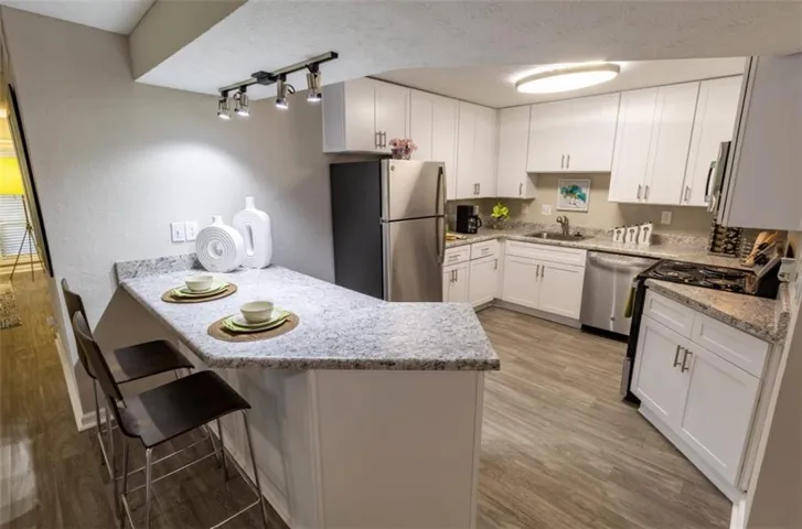 Kitchen featuring appliances with stainless steel finishes, a kitchen bar, white cabinets, a peninsula, and a textured ceiling