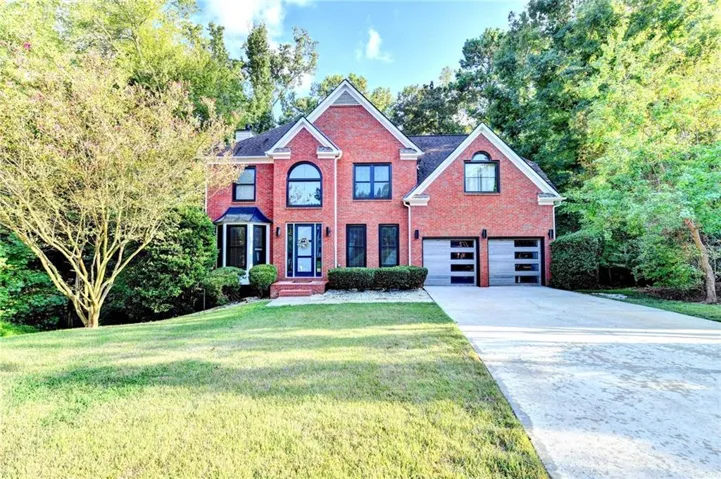 Red brick exterior with white trim, arched window, bay window, two-car garage with frosted glass doors, and a concrete driveway