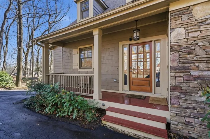 Doorway to property featuring a porch, roof with shingles, and stone siding