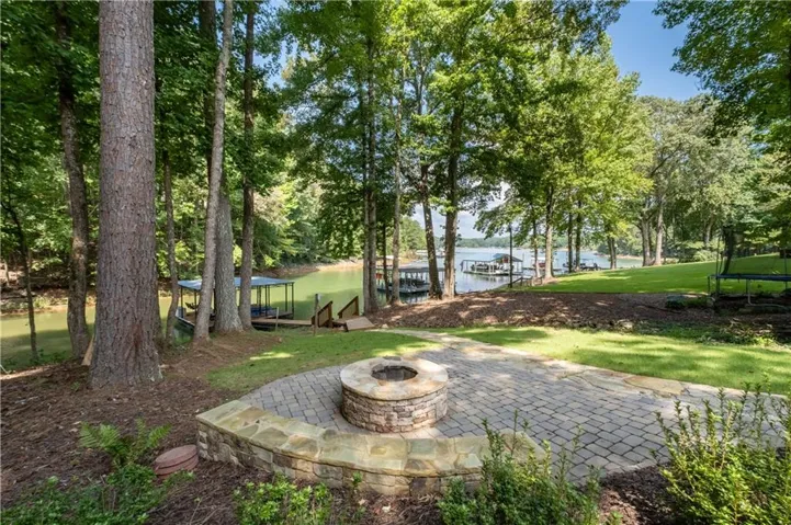 Paver patio featuring a stone fire pit, extensive green space, mature trees, and waterfront access with docks