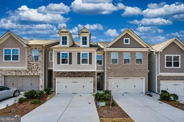 Modern townhome exterior featuring a two-car garage, brick and siding facade, dormer windows, and a concrete driveway