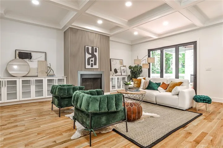 Spacious living area featuring coffered ceilings, recessed lighting, a fireplace with a slatted accent wall, built-in cabinetry with glass-front doors, and wood-finish flooring