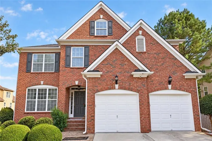 Brick exterior with white trim, featuring a two-car garage with arched brick detailing, dark shutters, and a covered entry