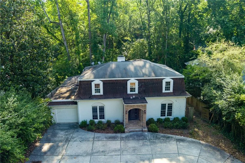 View of front facade featuring driveway, a garage, stucco siding, a chimney, and mansard roof