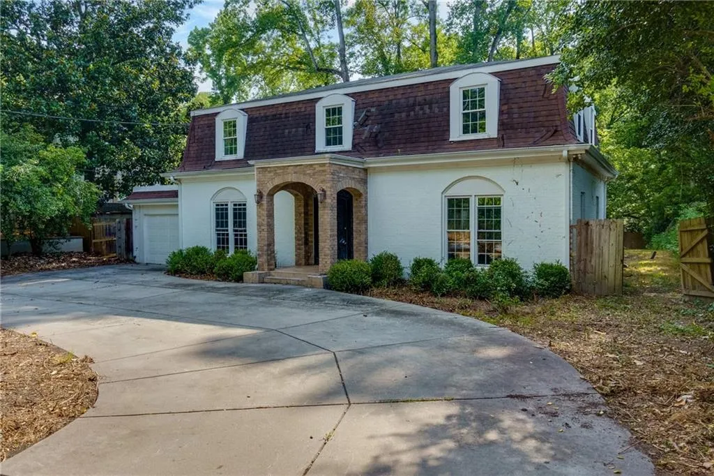 View of front of home featuring mansard roof, roof with shingles, a garage, and driveway