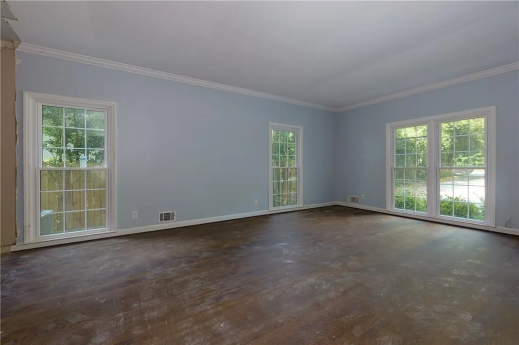 Empty room featuring crown molding, healthy amount of natural light, and dark wood-style floors