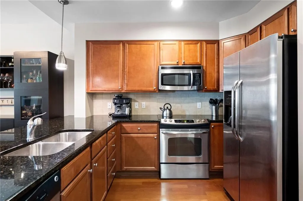 Kitchen with dark stone counters, appliances with stainless steel finishes, light hardwood / wood-style flooring, backsplash, and hanging light fixtures
