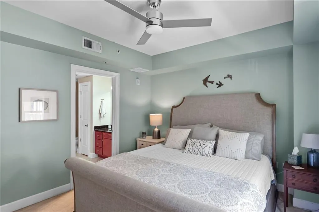 Bedroom with ceiling fan, connected bathroom, and light colored carpet