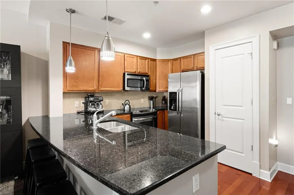 Kitchen featuring pendant lighting, dark stone counters, appliances with stainless steel finishes, backsplash, and dark wood-type flooring