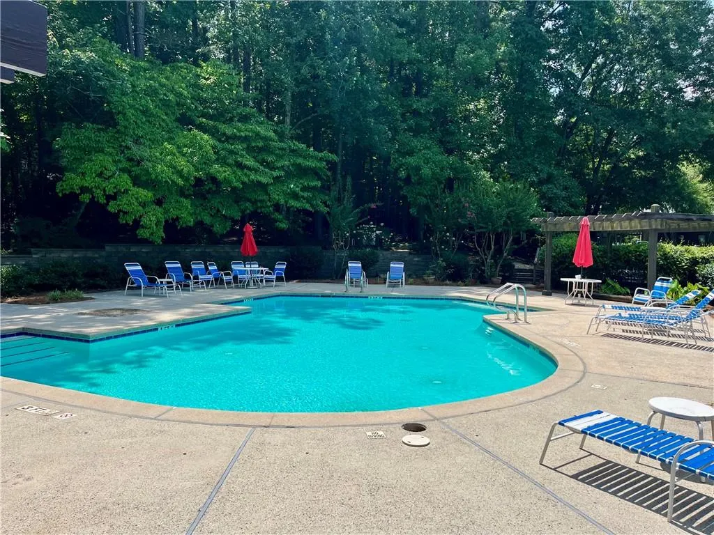 Community pool featuring a patio area, a pergola, and view of wooded area