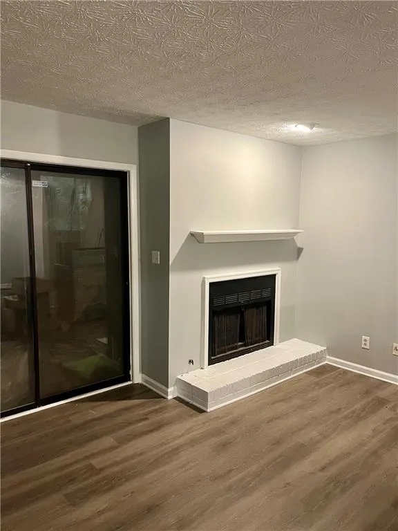 Unfurnished living room featuring wood finished floors, a brick fireplace, and a textured ceiling