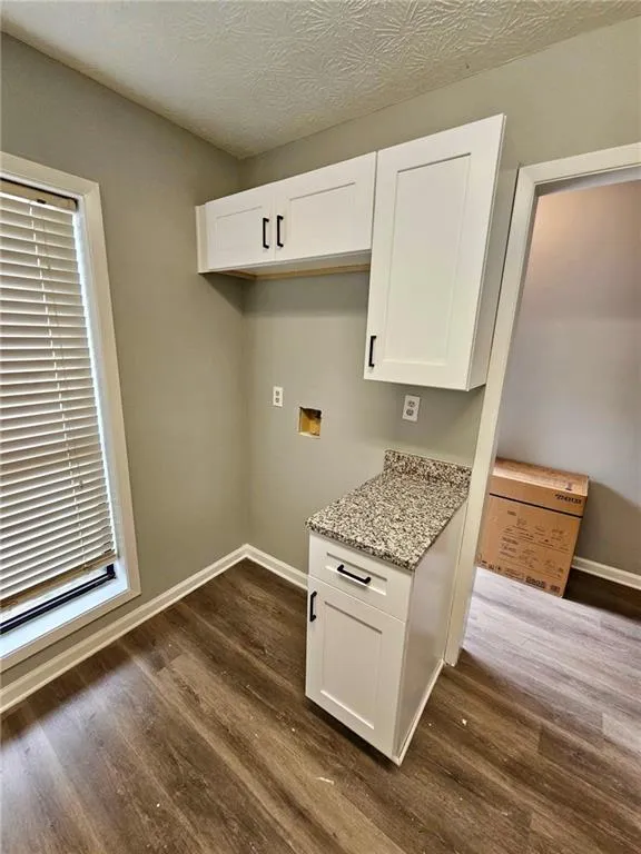 Kitchen with light stone counters, dark wood-style flooring, white cabinets, and plenty of natural light