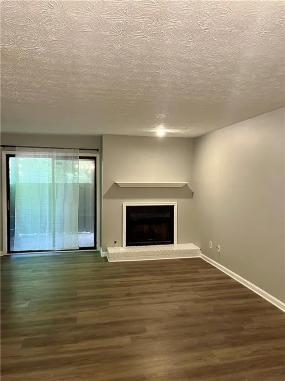 Unfurnished living room featuring wood finished floors, a brick fireplace, and a textured ceiling