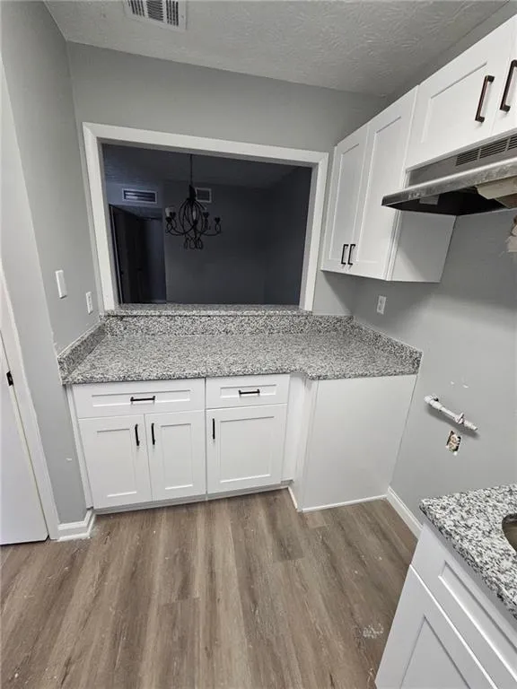 Kitchen featuring under cabinet range hood, wood finished floors, light stone countertops, and white cabinetry