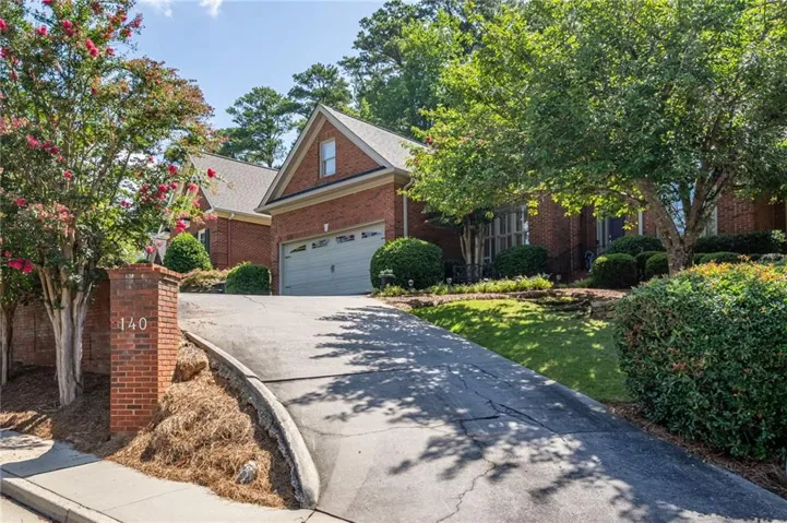 Brick exterior with an attached garage, featuring a gabled roofline, mature trees, and established landscaping