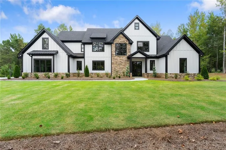 Modern farmhouse exterior featuring board-and-batten siding, stone accents, dark-framed windows, and a black shingle roof