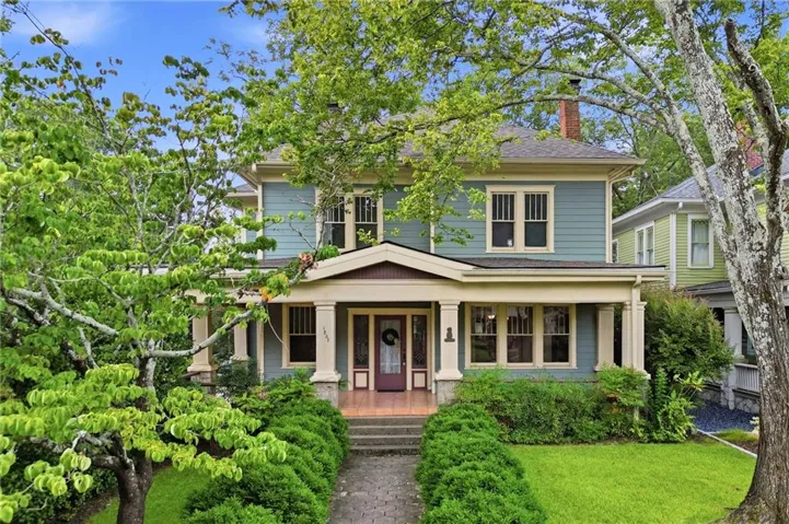 Two-story residence featuring light blue siding, a covered porch with pillars, and a red brick chimney