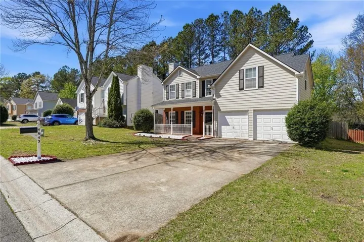 Traditional-style home with a porch, an attached garage, concrete driveway, a chimney, and a shingled roof