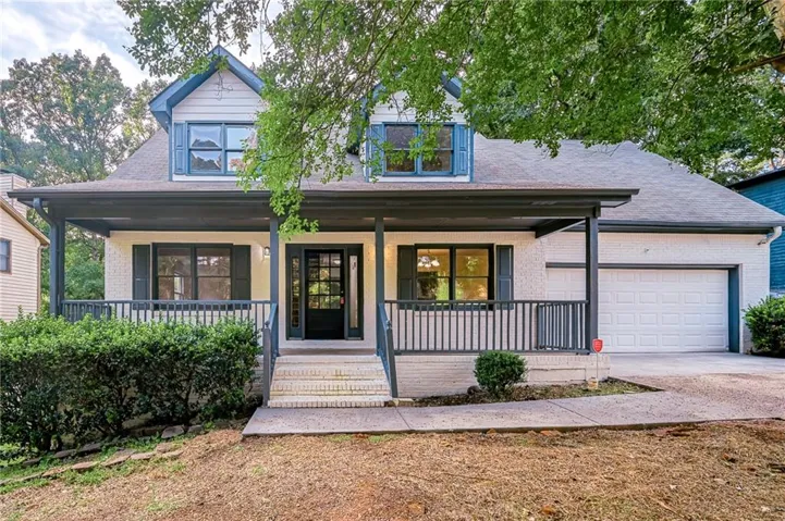 Two-story residence featuring a covered front porch, brick exterior, attached garage, and dormer windows