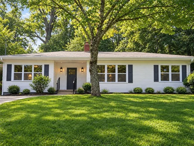 White horizontal siding exterior with dark shutters, dark entry door, and a brick chimney