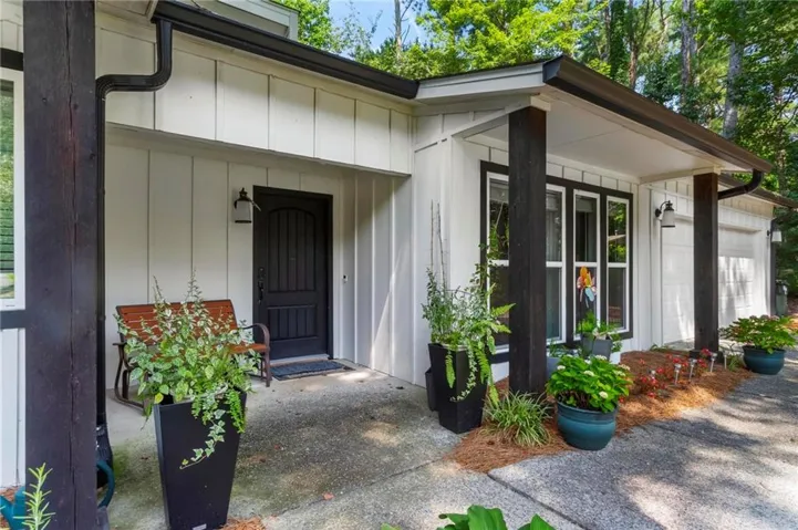 White vertical board siding, black-trimmed windows, dark wood support columns, arched panel front door, and exterior lighting fixtures