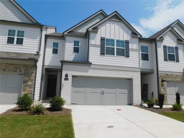 Contemporary townhome with a white siding exterior, stone accents, a two-car garage, and a concrete driveway