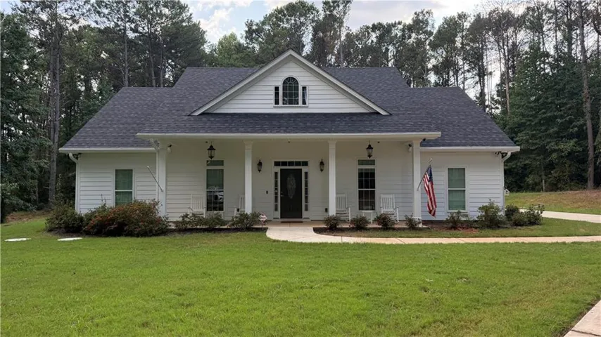 White siding exterior with a dark shingle roof, a covered front porch with columns, a prominent front gable, and an arched window dormer