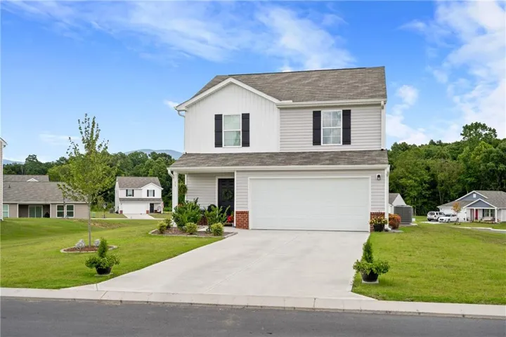 Two-story residence with a light gray and white facade, an attached garage, a concrete driveway, and front landscaping