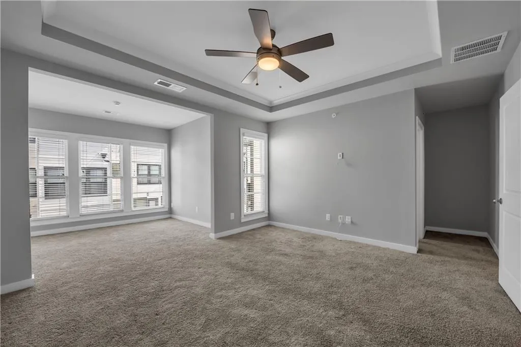 Carpeted empty room with a tray ceiling and ceiling fan
