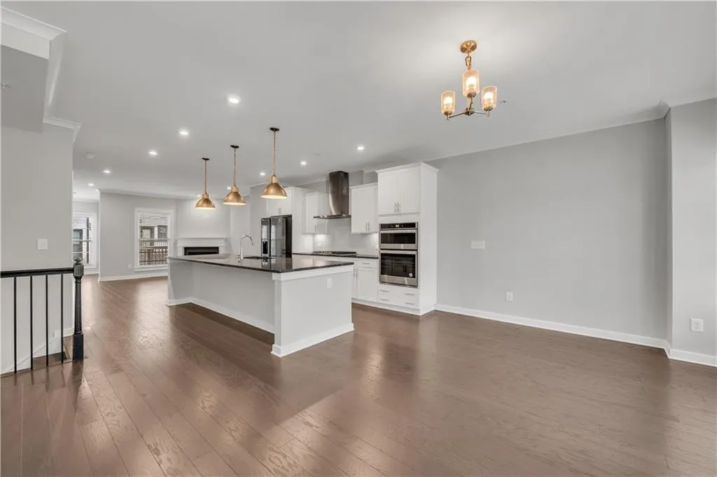 Kitchen with wall chimney range hood, stainless steel appliances, dark countertops, dark wood finished floors, and open floor plan