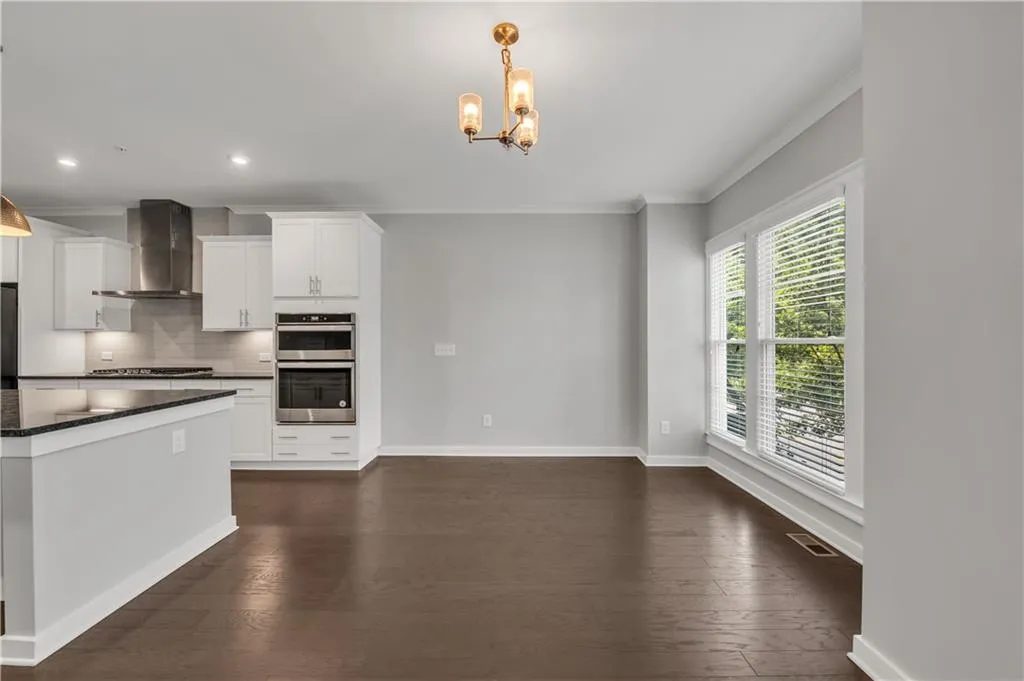Kitchen with wall chimney exhaust hood, double oven, cooktop, dark countertops, and a chandelier