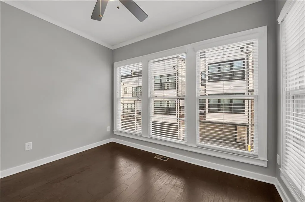Empty room featuring a ceiling fan, dark wood-style floors, healthy amount of natural light, and ornamental molding