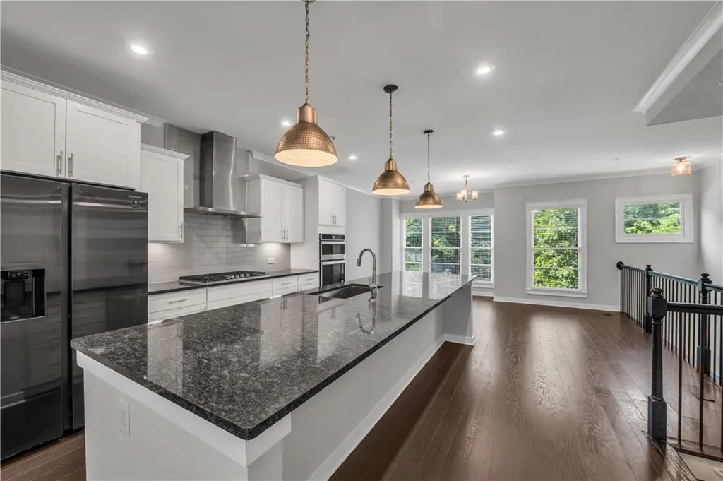 Kitchen with wall chimney range hood, appliances with stainless steel finishes, tasteful backsplash, a large island, and white cabinetry