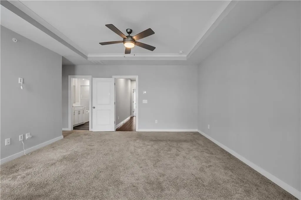 Unfurnished bedroom with a tray ceiling, carpet flooring, ensuite bathroom, ornamental molding, and a ceiling fan