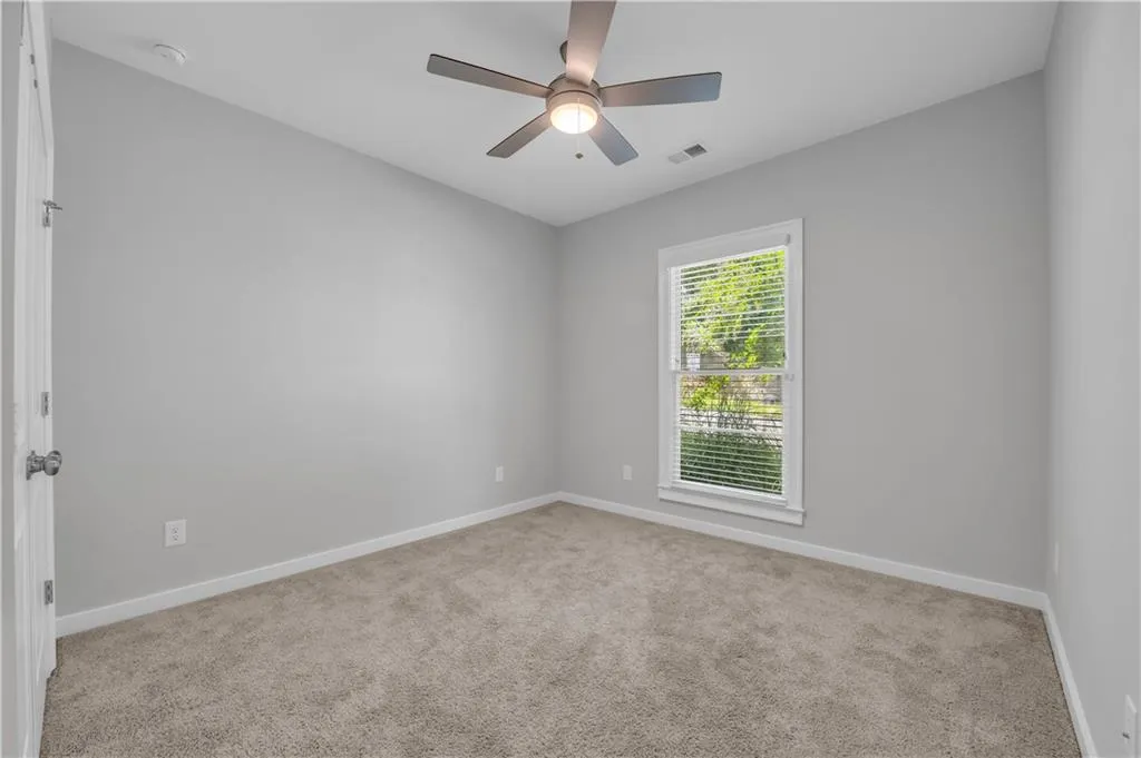 Carpeted empty room featuring a ceiling fan and a smoke detector
