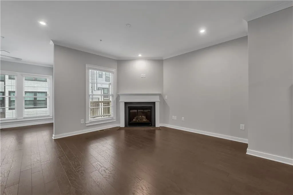 Unfurnished living room featuring ornamental molding, dark wood finished floors, a fireplace with flush hearth, and recessed lighting