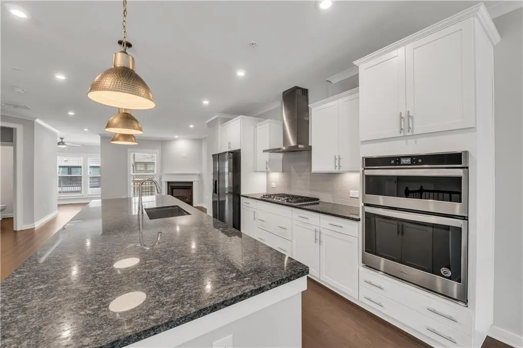 Kitchen with wall chimney range hood, stainless steel appliances, backsplash, a spacious island, and white cabinetry