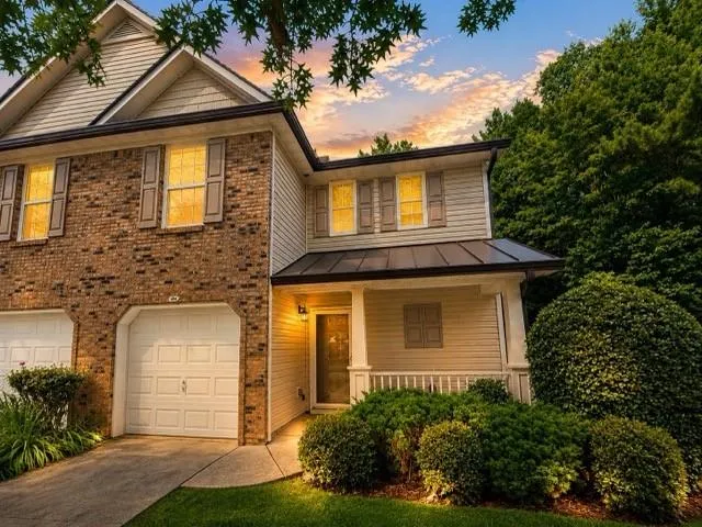 Brick and siding exterior with a covered entry, attached garage, and mature landscaping