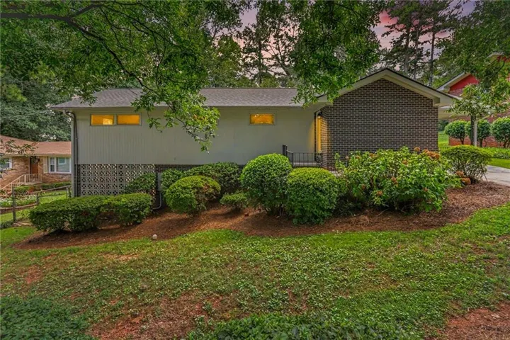 Brick exterior with a shingled roof, mature trees, and established shrubbery