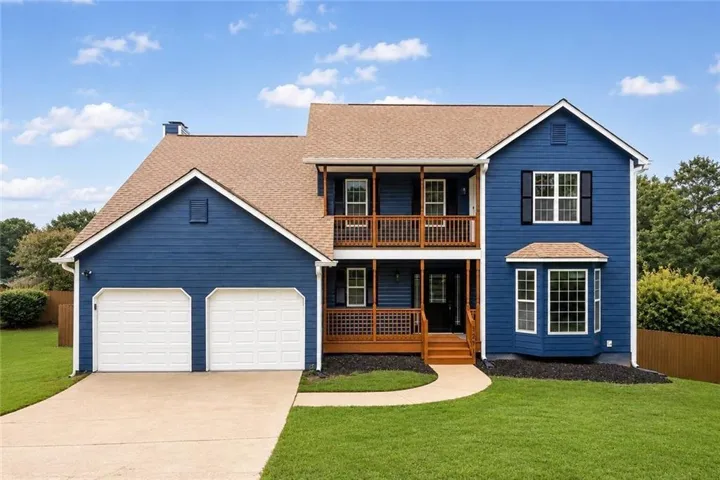 Blue siding exterior with a two-car garage, upper and lower-level balconies, and a ground-floor bay window