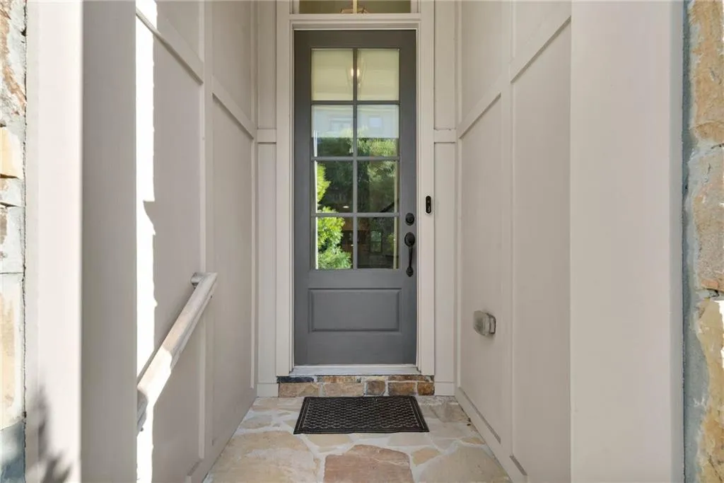 Covered entryway featuring a six-panel glass door with transom window, flagstone flooring, board and batten siding, and natural stone accents