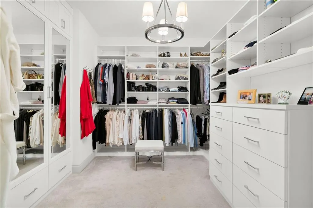 Custom-built white cabinetry with extensive shelving, integrated mirrored wardrobe doors, a multi-drawer storage unit, and a central circular light fixture