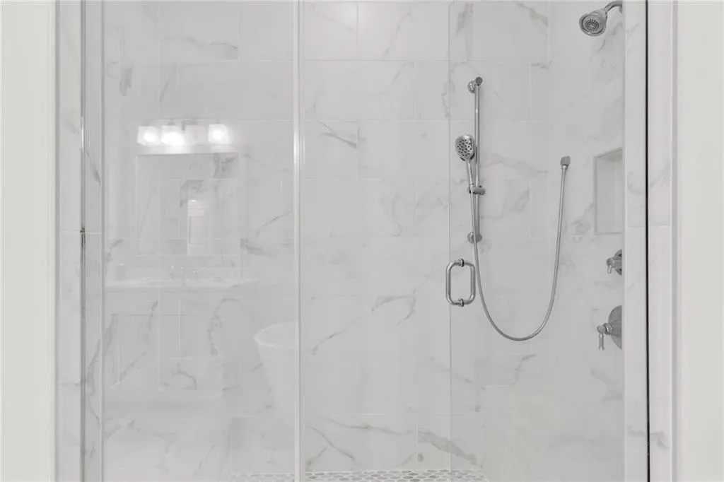Walk-in shower featuring floor-to-ceiling stone-finish tile, glass enclosure, built-in recessed wall niche, adjustable handheld shower head, and mosaic tile floor inlay