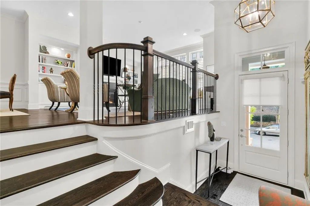 Entryway featuring wood-finish stairs with white risers, dark wood railings with vertical metal balusters, integrated wall cabinetry, and a geometric pendant light fixture
