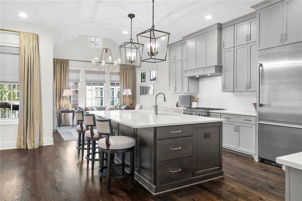 Kitchen featuring a center island with quartz countertop, dark-finish cabinetry, stainless steel refrigerator, white tile backsplash, and oversized metal pendant lighting