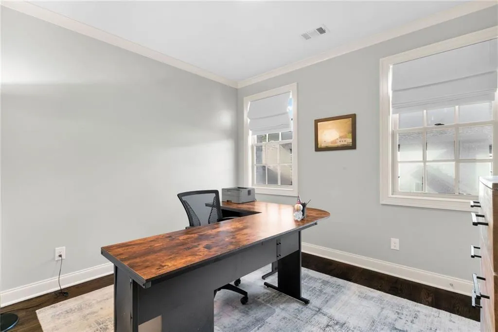 Room featuring dark wood-finish flooring, crisp crown molding, and two windows with multi-pane grid detailing