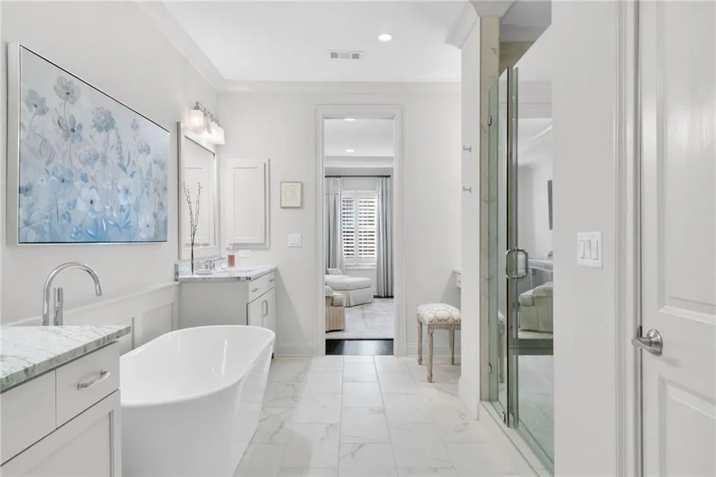 Freestanding soaking tub, dual-sink vanity with stone countertop, walk-in glass-enclosed shower, and large-format tile flooring