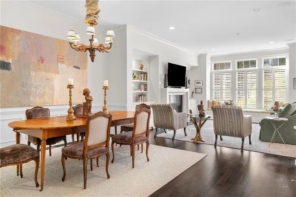 Open-concept interior featuring dark wood-finish flooring, a traditional chandelier, built-in shelving, a fireplace with a mantel, and windows finished with plantation shutters