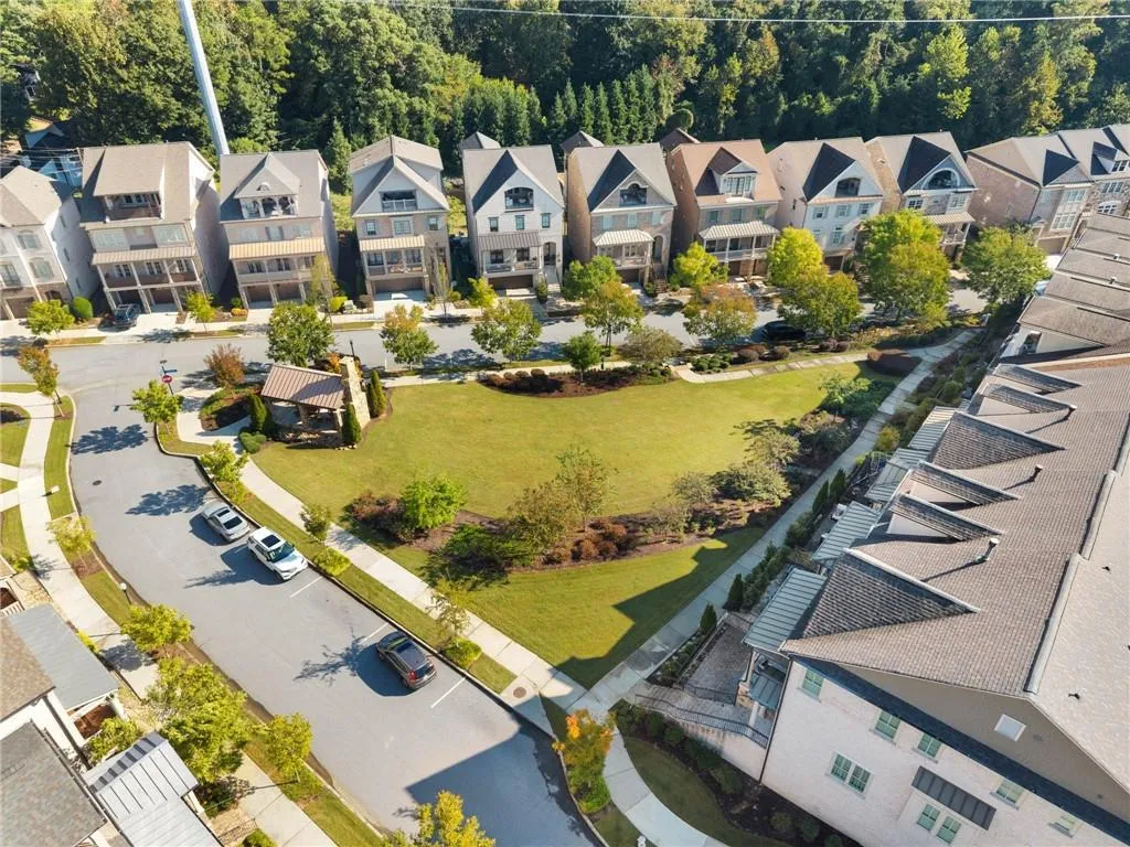 Aerial perspective of a multi-unit residential community featuring asphalt roadways, concrete sidewalks, a central landscaped park area, and a stone-accented gazebo